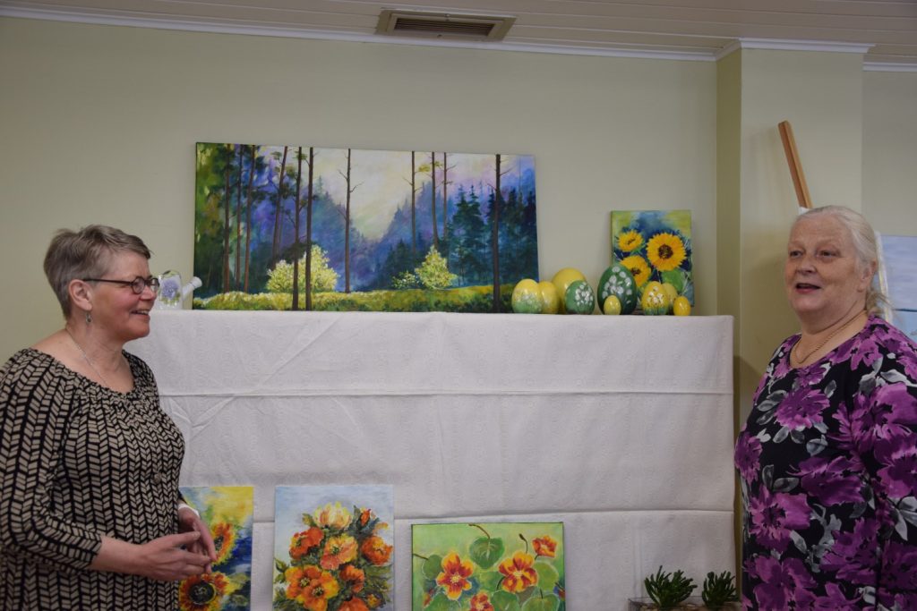 Sirpa Kataja ja Kirsti Jaakkola kokosivat Katajan kuvataide- ja posliinimaalausryhmien kevätnäyttelyn. Taustalla Jaakkolan maalaus.