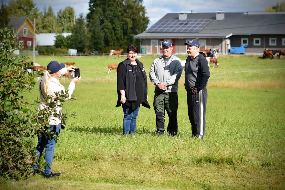 Ministerin avustaja Annukka Annala otti kuvan, kun Hanne ja Arto Tyynismaa ja Antti Kurvinen poseerasivat lehmät ja navetta taustallaan.