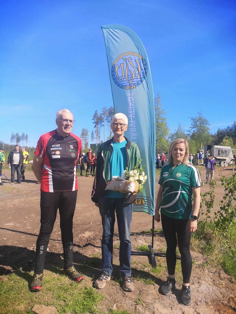 Tapio Patana (vas.) ja Pia Suomela muistivat kisapäivän sankaria Voitto Erkinheimoa kukkasin ja ojensivat hänelle hopeisen ansiomitalin.