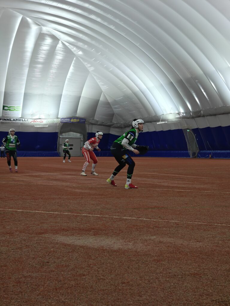 Alajärven Pallohalli tarjoaa kesäiset olosuhteet pesäpallo-otteluille myös talvella. Maria Lahti numerolla 5, sekä taustalla Elli Kangas ja Elise Lähdemäki yrittävät katkaista Jussien vaihtoyrityksen. Kuva: Piritta Kärnä.