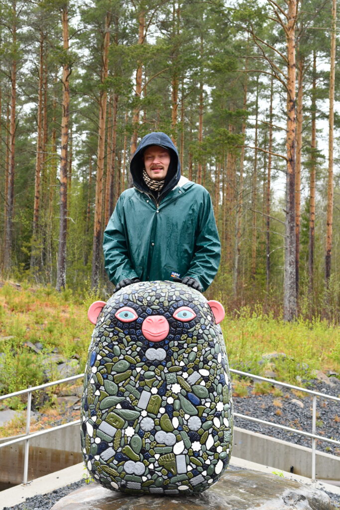 Taiteilija Ville Heimala nykyaikaa kuvastavan teoksensa kanssa. Teos sijaitsee Välijoen laavun pihassa.
