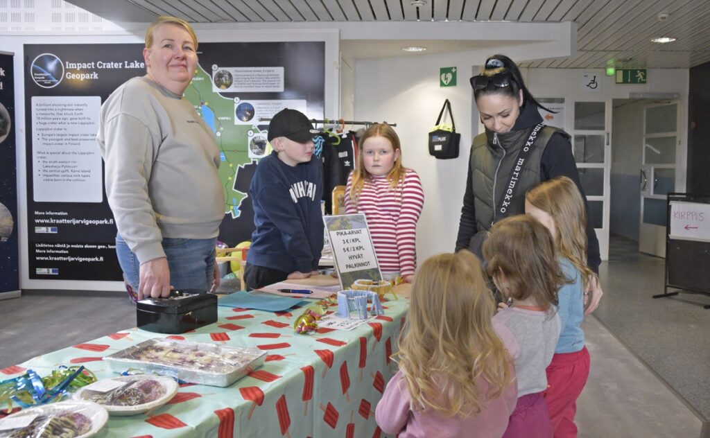 Anna Angervisto (vas.), Eemeli Angervisto ja Pihla Saari myivät arpoja Rovastilan kyläyhdistyksen pisteellä. Kauhavalainen Mari Kankaanpää osti lapsille arpoja.