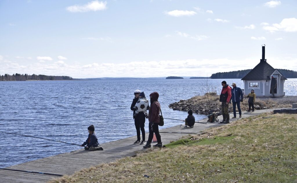 Lapset ja aikuiset kalastamassa Kirpun laiturilla. Kodassa loimotti iloisesti lämmin valkea.