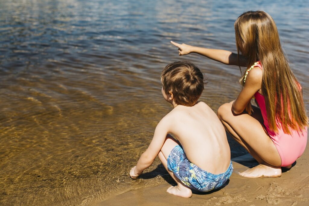 Girl sitting with boy pointing away coastline