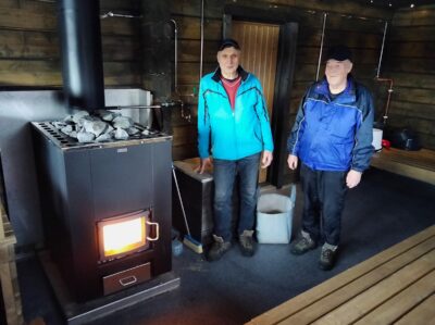Jukka Kuusela ja Hannu Soisalo kuuluvat saunan lämmittäjäkaartiin. Puolentoista tunnin lämmitysaika uudessa saunassa on ollut iloinen yllätys, pidempään oli varauduttu.