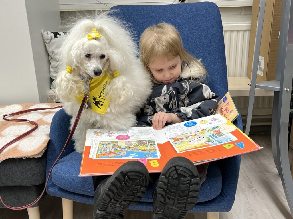 Helmi lukee ja lukukoira Mindi kuuntelee Evijärven kirjastossa.