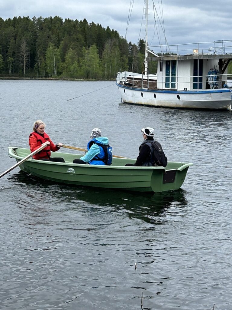 Kyrönsaareen on rakennettu hyvä laituri, mutta matalan vedenpinnan takia veneestä ei päässyt suoraan laiturille. Soutajana Eeva-Maija Savola ja kyydissä Sinikka Paalanen ja Ritva Vistinmäki. Taustalla Unelma-laiva. Kuva: Virpi Nokua.