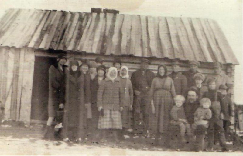 Purmon Kauhajärveläisiä vierailulla Roismassa maaliskuussa 1931.     Perheeseen oli syntynyt pokavauva, ja kyläläiset olivat sen vuoksi               onnittelukäynnillä. Matti istuu kuvan keskellä lapset polvellansa ja Amalia      seisoo hänen vierellään . Mökki oli tuolloin vielä hyvin alkeellinen. Kuva: Anna-Liisa Björklund.
